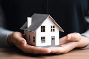 a imagem remete a conquista da casa por meio do consórcio de imóveis, na imagem o homem segura uma casa com a palma das mãos